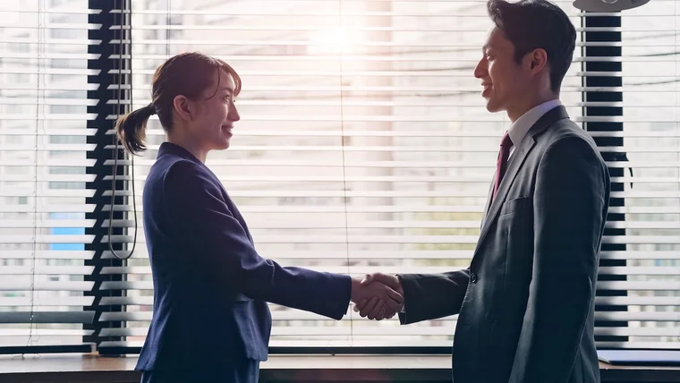 Two corporate employees shake hands while smiling