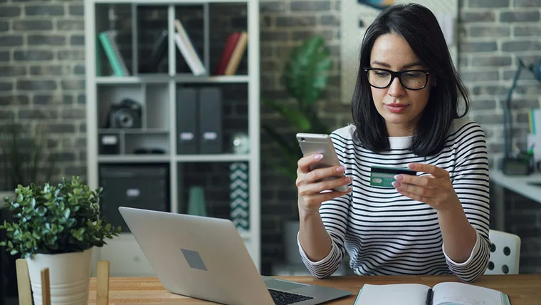 A woman sits in front of her laptop with a credit card and phone in head, ready to donate online.