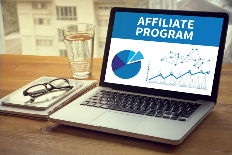 A laptop sits on a table with a pie chart and grid on it's screen accompanied by the words "Affiliate Program"