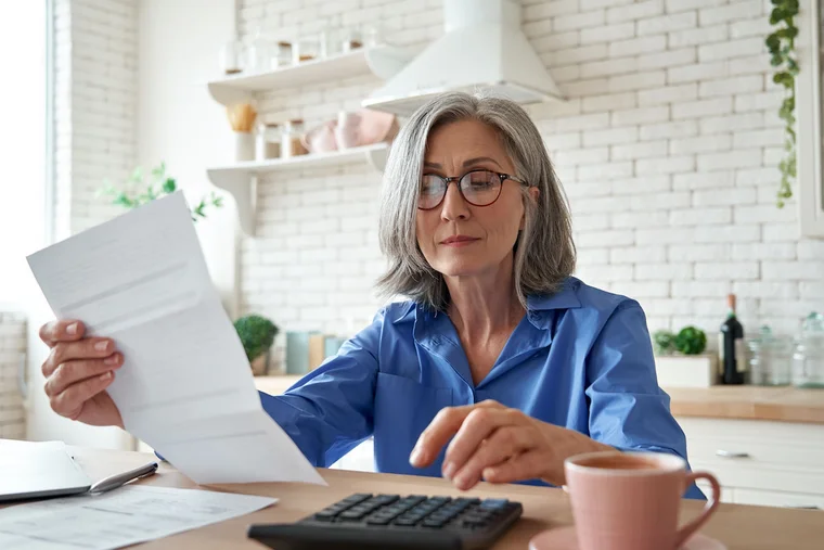 A woman sits in her kitchen at her laptop, reviewing documents
