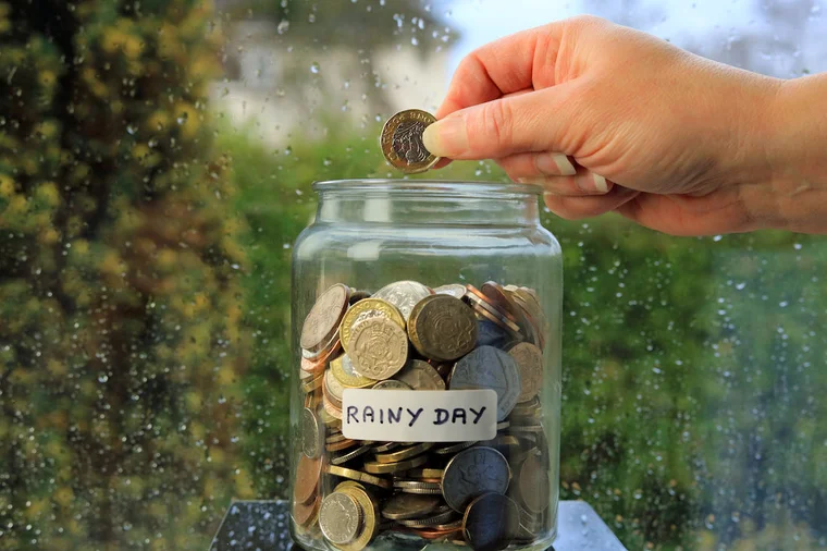 someone placing a coin into a jar labeled rainy day fund