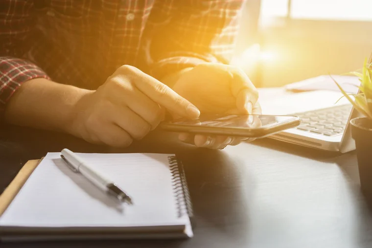 Close up of someone scrolling on their phone at a work desk