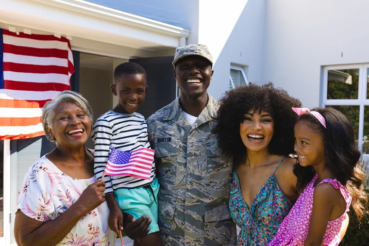 A military family smiling outside, in front of a flag.