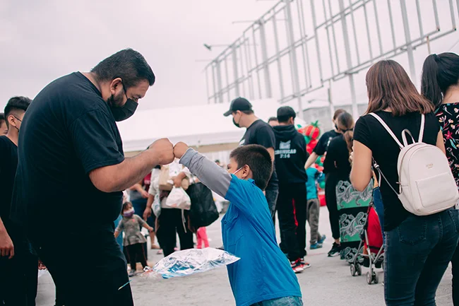 A man in a mask fist bumps with a child in a mask outside of an event