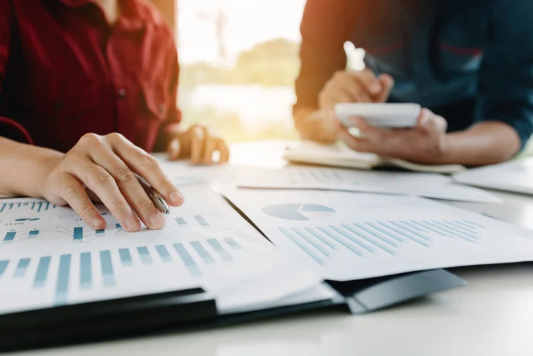 Close-up of two people working together at a table with charts and graphs