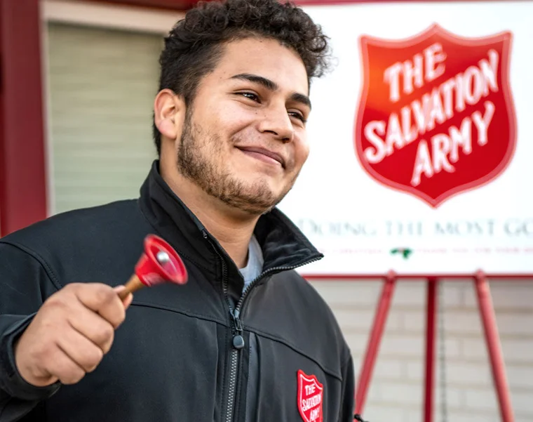 A gentleman rings a bell outside in front of a sign that reads "The Salvation Army"