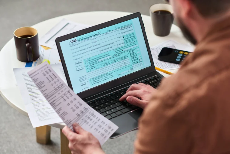 Over the shoulder shot of someone doing taxes, holding a receipt and filling out a tax form online