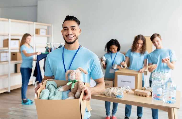 A group of smiling volunteers sort through donations while organizing into boxes