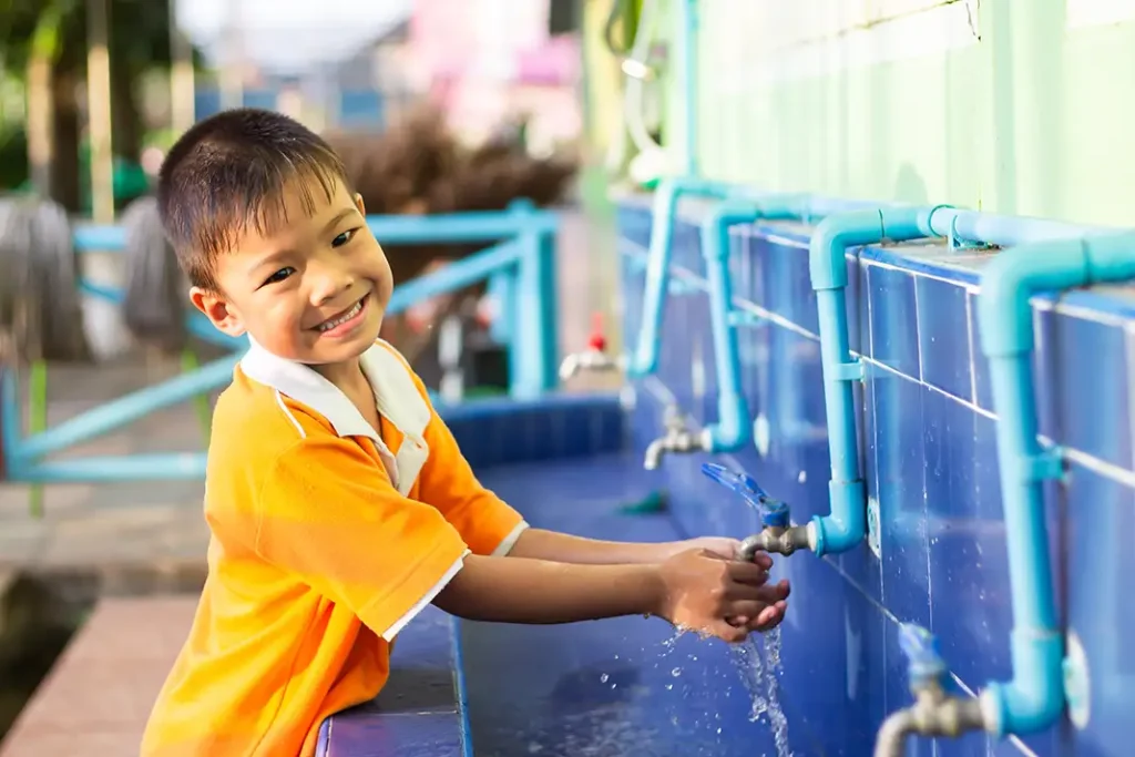 Young boy smiling while washing hands at an outdoor sink at the park